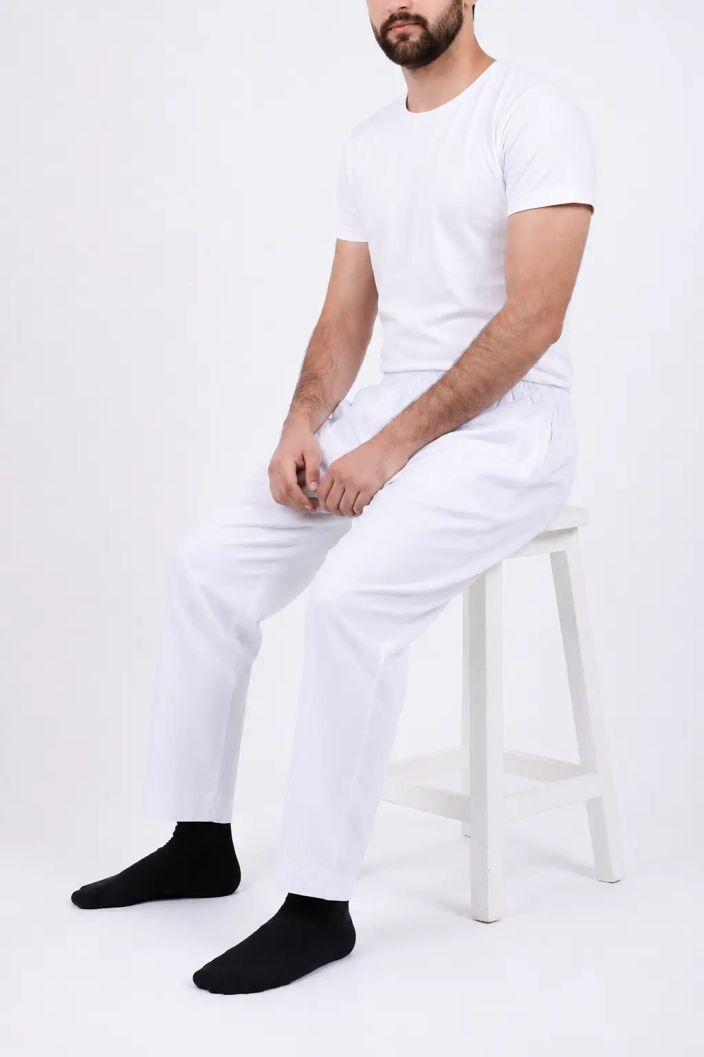 ChatGPT Image Jul 1, 2026, 02_53_32 PM (4) Man in a plain white T-shirt and white lounge pants sits on a white stool, wearing black socks against a white background.