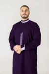 Man in a deep purple traditional thobe with lavender trim, standing against a light gray background.