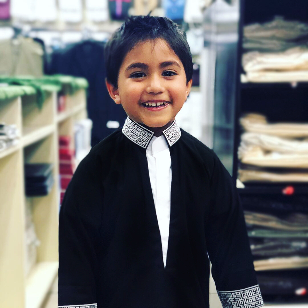 Custom-tailored kids' thobe in black and white. Features unique geometric embroidery on the collar, designed using the al qamees DYO platform for boys.