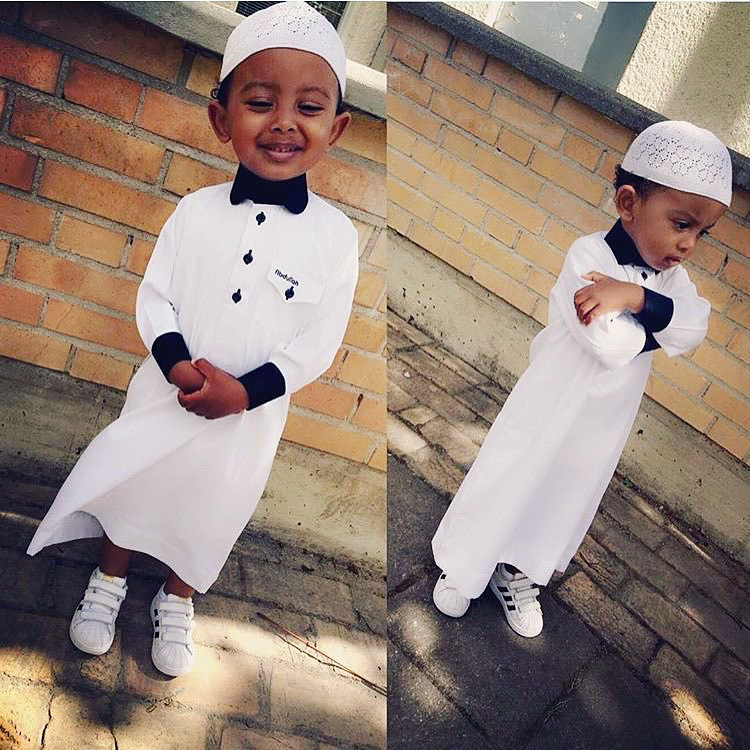 Personalized kids' thobe in white with black contrast detailing. Bespoke alqamees DYO design for children featuring custom embroidery and name tags.