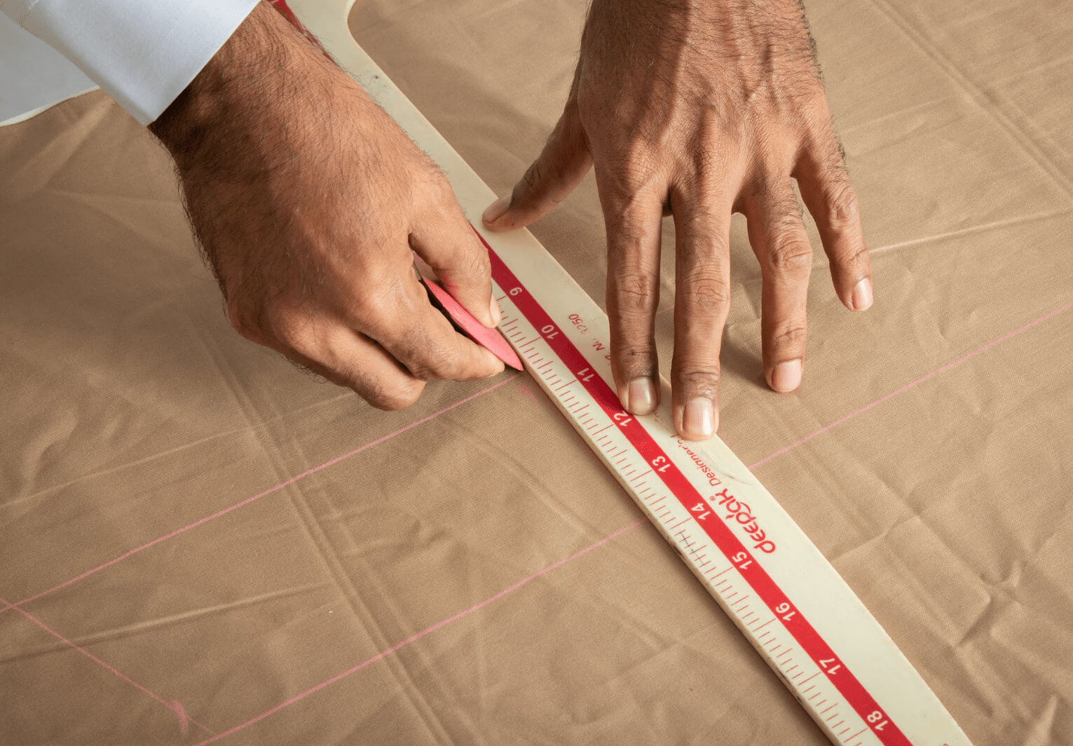 Expert tailor hand-marking premium fabric with chalk and ruler for a custom-fitted thobe at alqamees