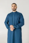 Men’s teal blue thobe with geometric embroidery by alqamees. A ready-to-wear thobe featuring a tailored fit, custom embroidered placket and cuffs, and a classic mandarin collar from the alqamees signature collection.