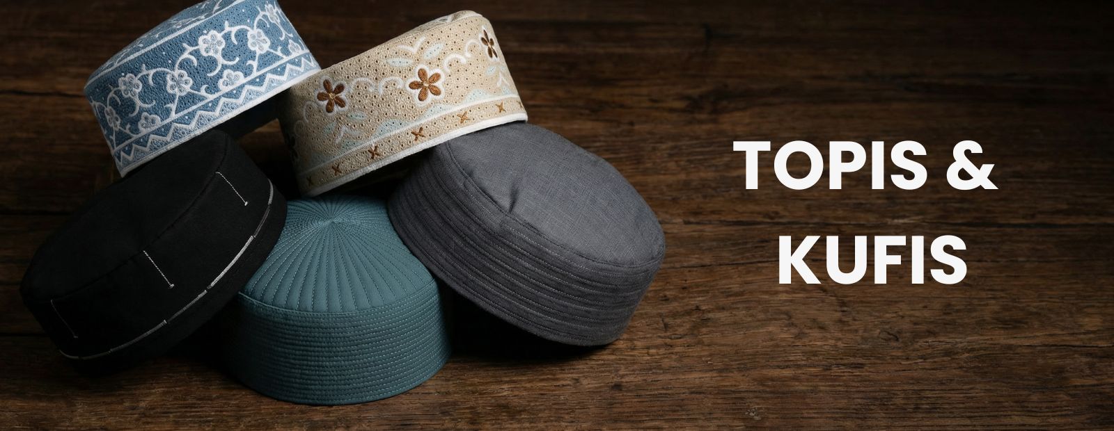 Assorted embroidered Topis and Kufis in blue, cream, black, and grey on a rustic wooden surface – alqamees prayer caps.