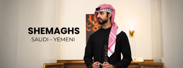 Man in a black traditional thobe and red‑and‑white shemagh stands indoors beside bold 'SHEMAGHS SAUDI - YEMENI' text, promoting the product.