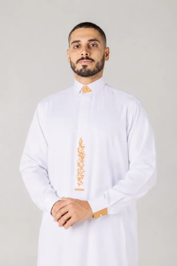 Man with short dark hair and beard wearing a white thobe with orange decorative trim, standing with hands clasped in front.