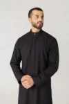 Man wearing a black thobe with a subtle patterned front panel, standing with hands clasped.