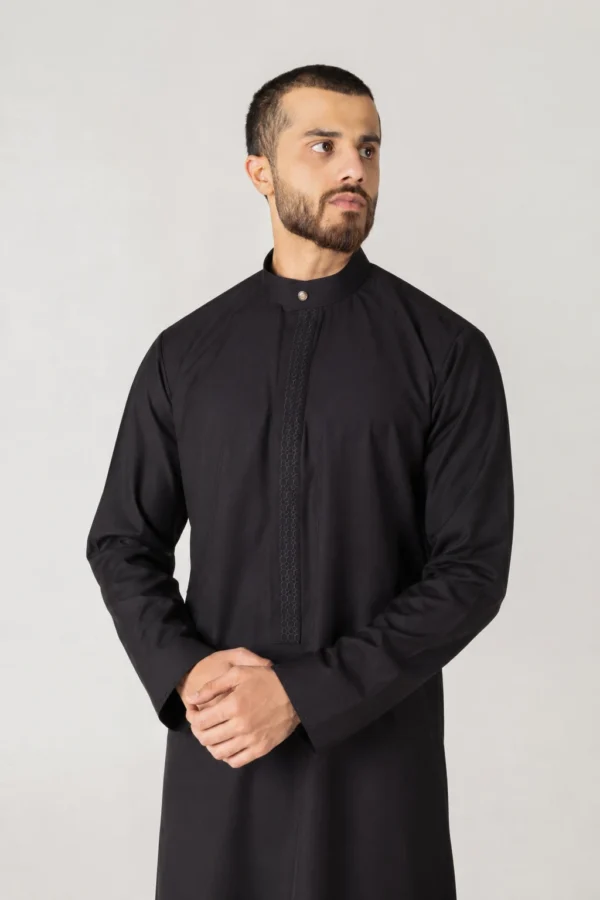 Man wearing a black thobe with a subtle patterned front panel, standing with hands clasped.