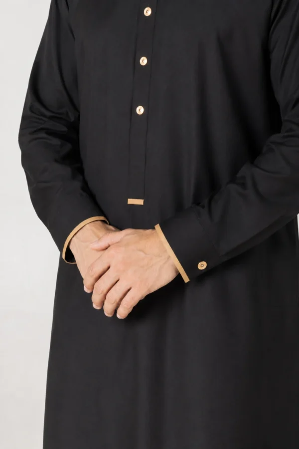 Close-up of a person wearing a black abaya with beige trim and gold buttons, hands folded in front of them