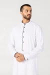 Man in a white thobe with black piping along the placket, cuffs, and neck, standing against a light background.