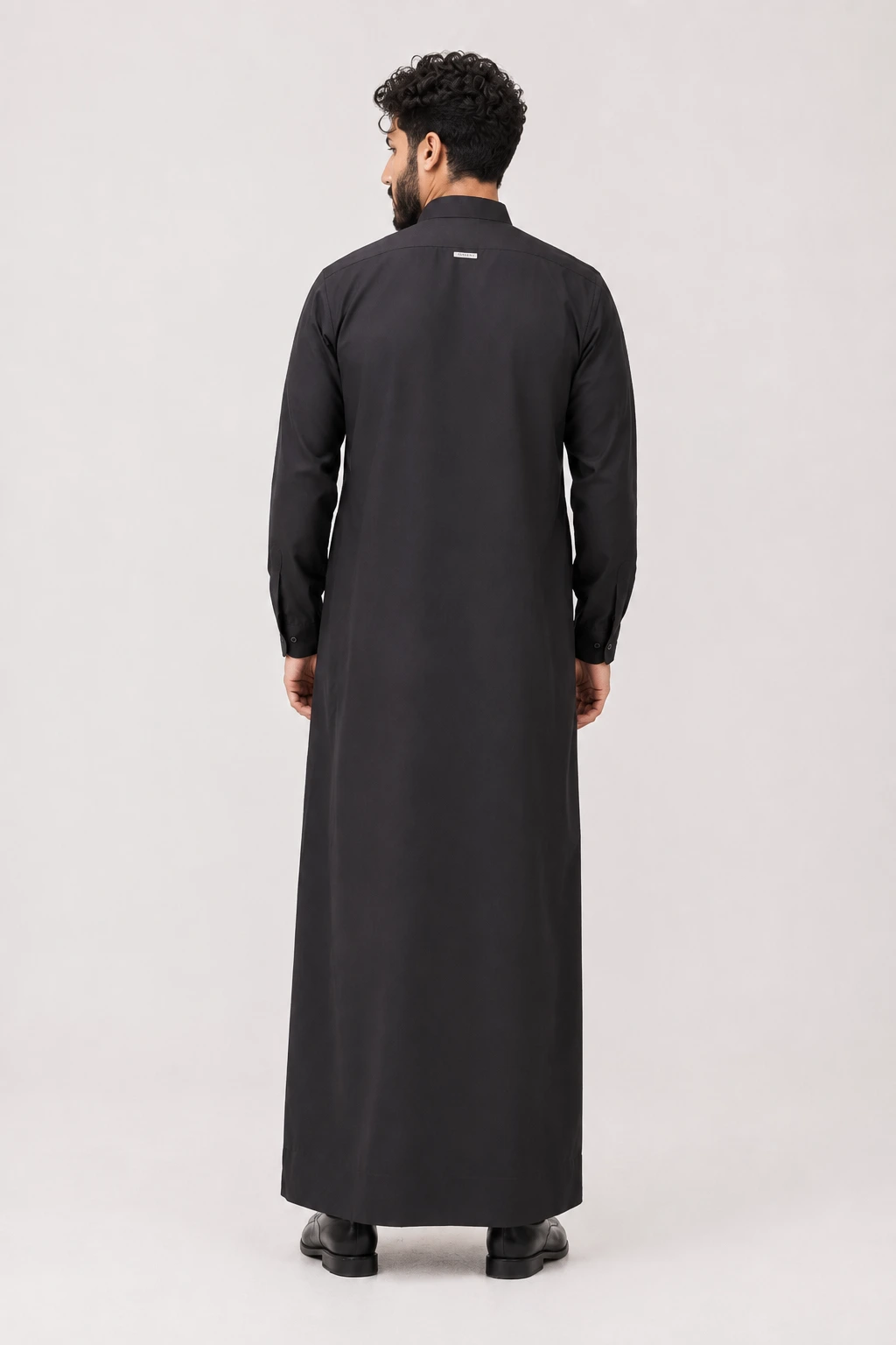 Backhour Black (2) Man wearing a long black thobe seen from the back, ankle-length with buttoned cuffs and a small label on the upper back