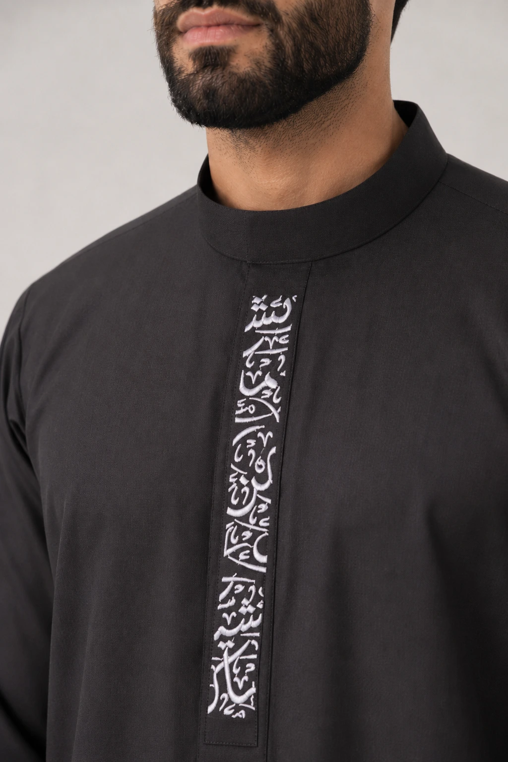 Backhour Black (4) Close-up of a man wearing a black thobe with a vertical white Arabic calligraphy panel down the front.