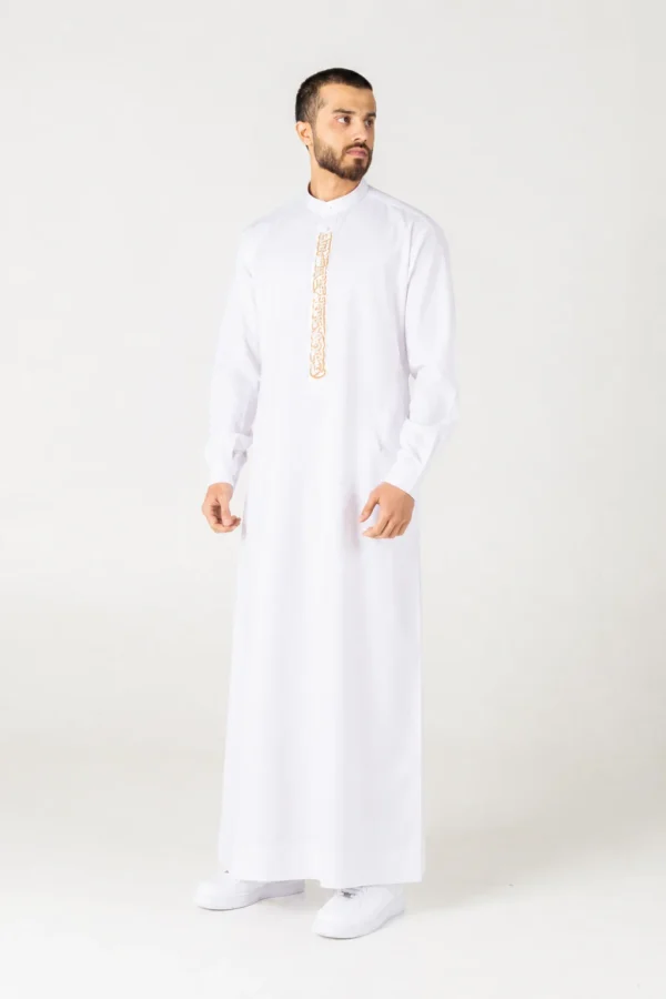 Man in a white thobe with gold embroidered vertical placket, standing against a light background.