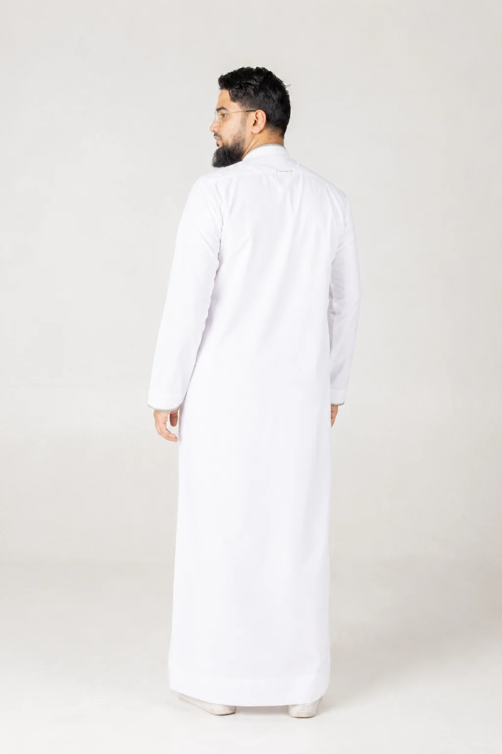 Nexus 7 Back view of a man wearing a long white thobe in a neutral studio backdrop, facing away from the camera.