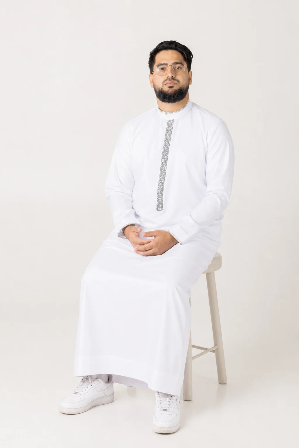 Nexus white 3 Man in a white kurta with decorative placket, seated on a stool against a light background.