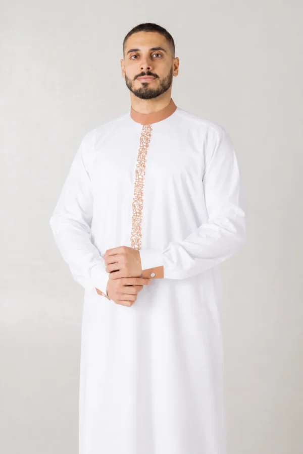 Man in a white kandura with beige embroidered trim down the front and on the cuffs, hands clasped in front.