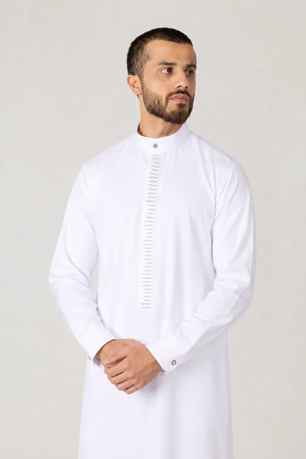 Rasasi White Edition (2) Man wearing a white kandura-style traditional robe, standing with hands folded, neutral studio backdrop