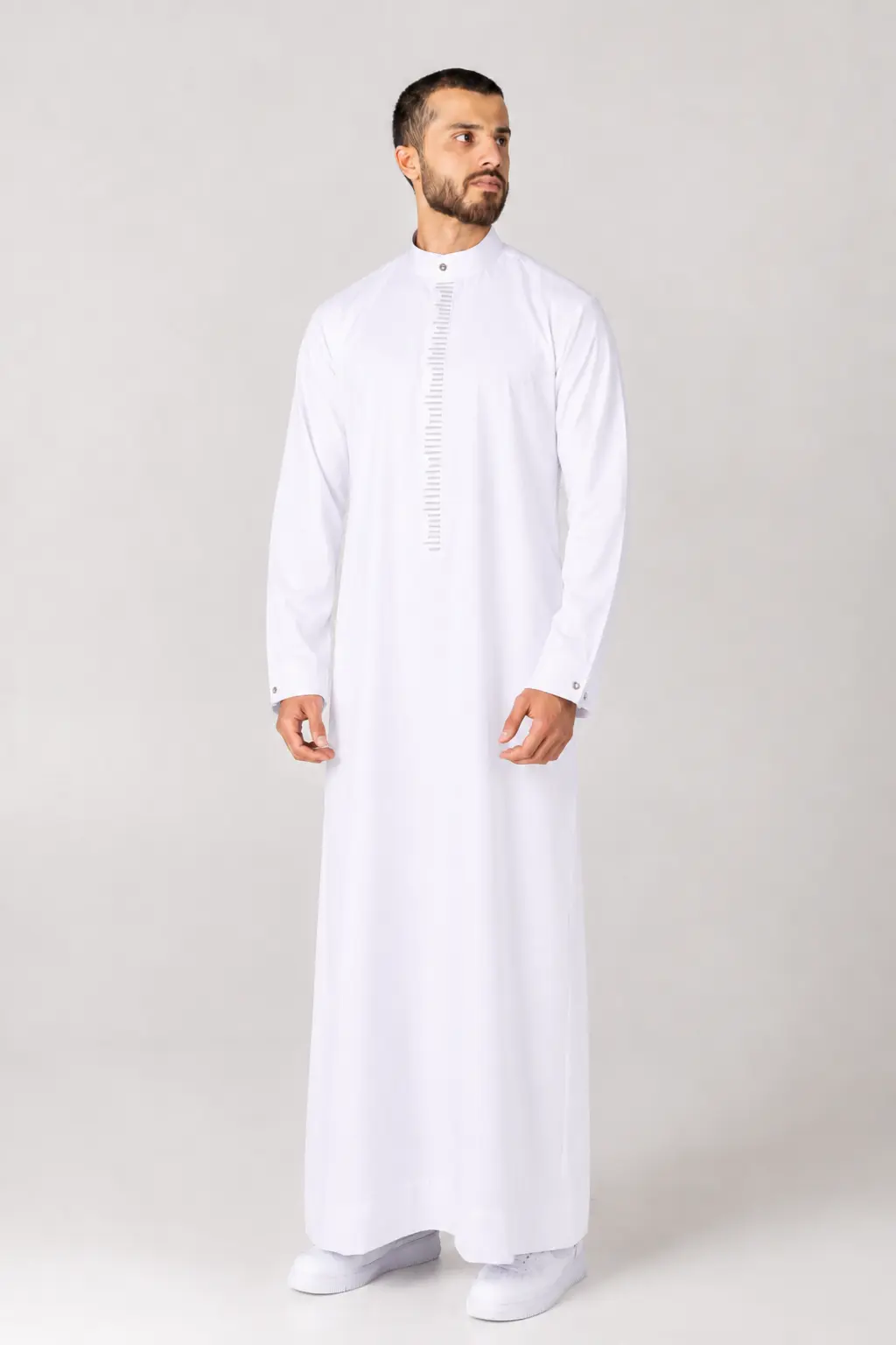 Rasasi White Edition (3) Man in a full-length white thobe with a stand-up collar and vertical decorative placket, looking to the right against a neutral background.