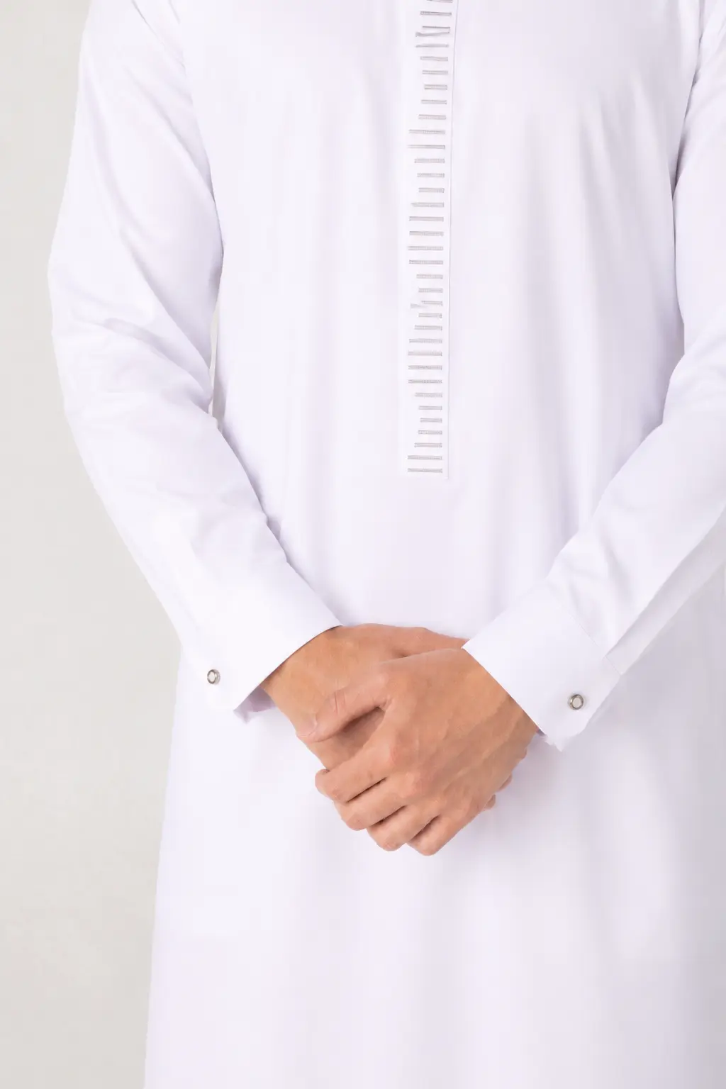 Rasasi White Edition (5) Man wearing a white thobe with a vertical ruler-like design down the front and hands clasped in front.