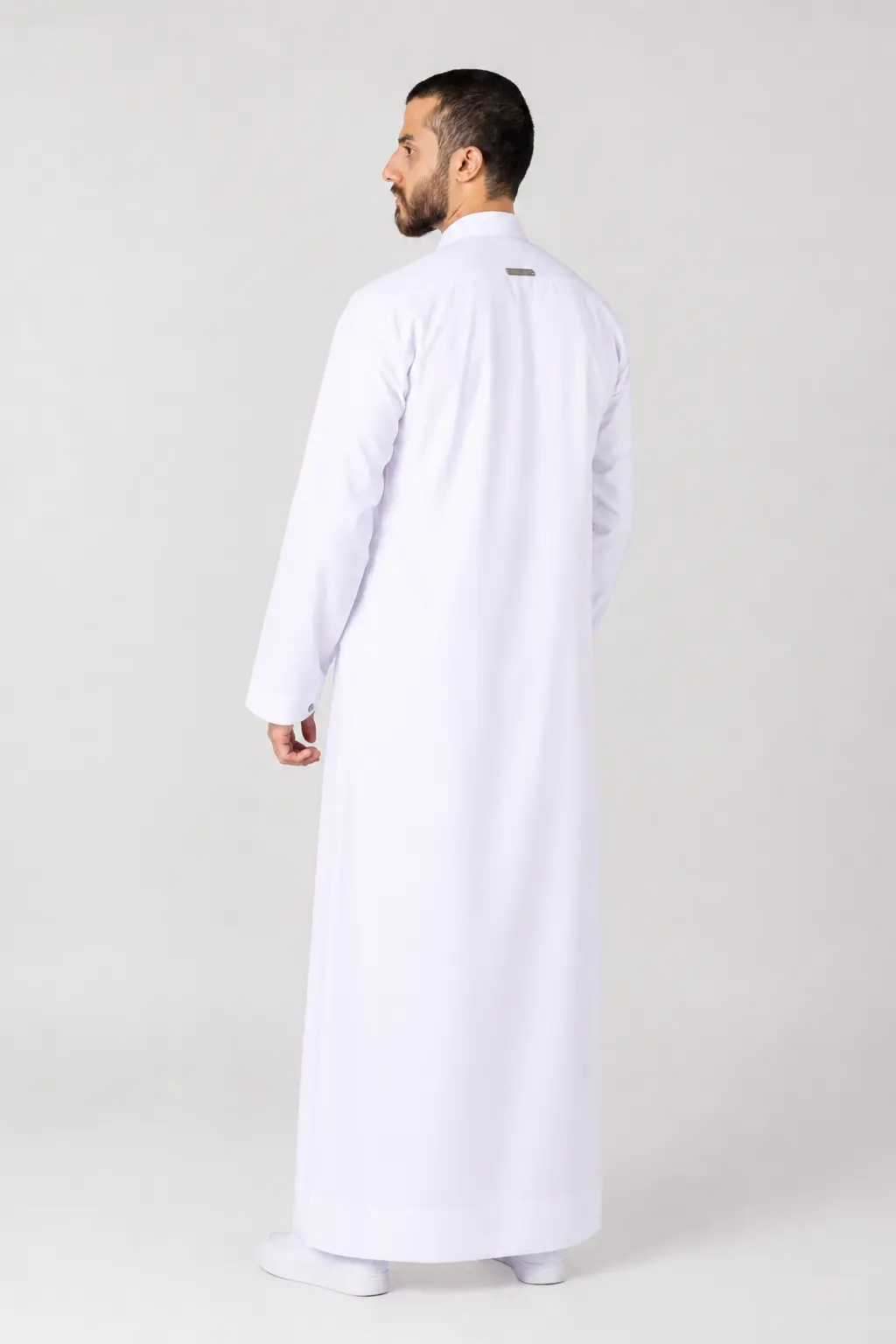 Rasasi White Edition Back view of a man in a full-length white thobe standing against a light gray background.