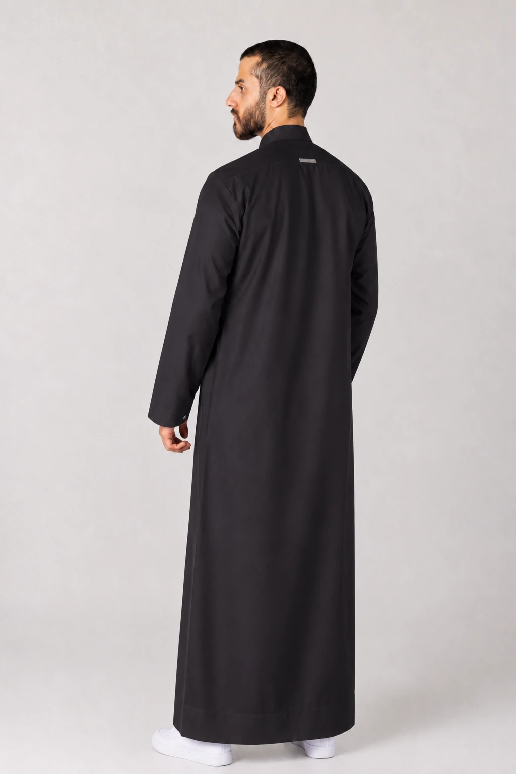 Rasasi Black Edition Man wearing a full-length black thobe seen from the back, standing with white sneakers visible at the bottom.