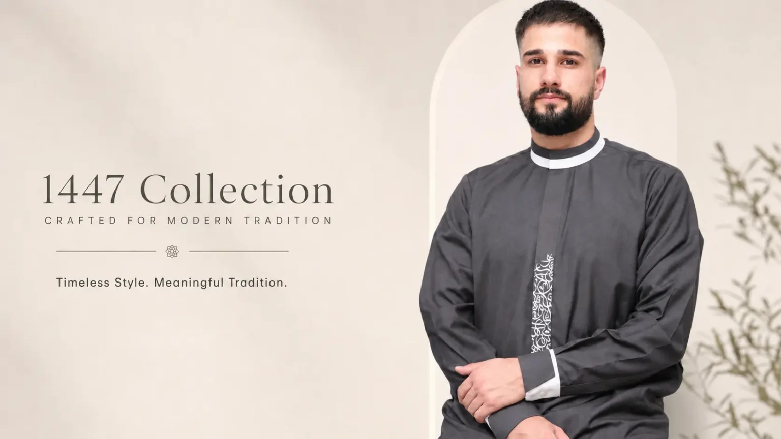 Man in a dark grey traditional robe posing beside a beige advertisement backdrop for the 1447 Collection.